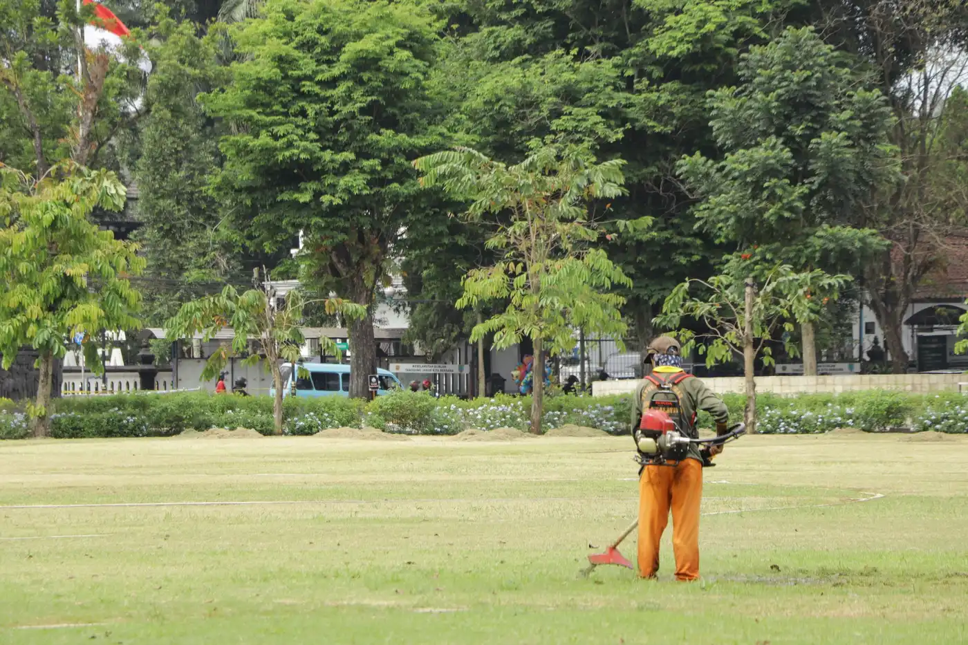 Grounds crew member trimming grass with a string trimmer on a large open lawn
