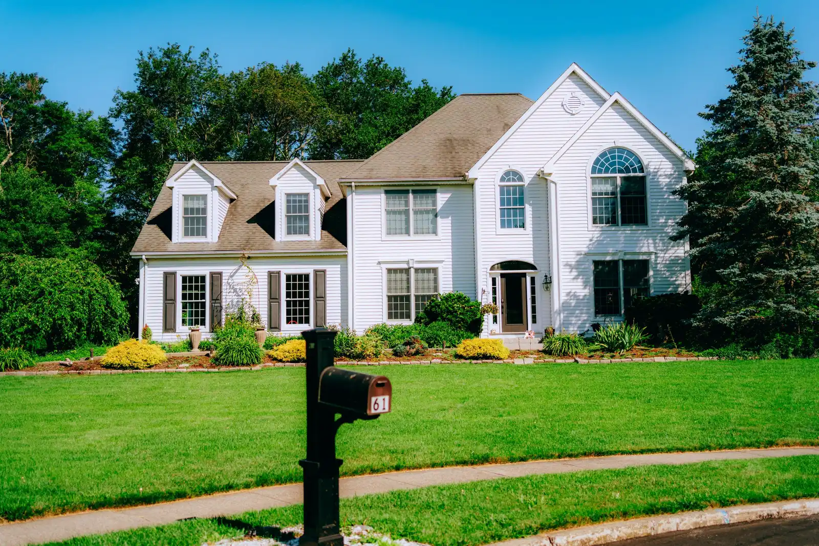 White two-story New England colonial home with a freshly mowed front lawn and planted foundation beds