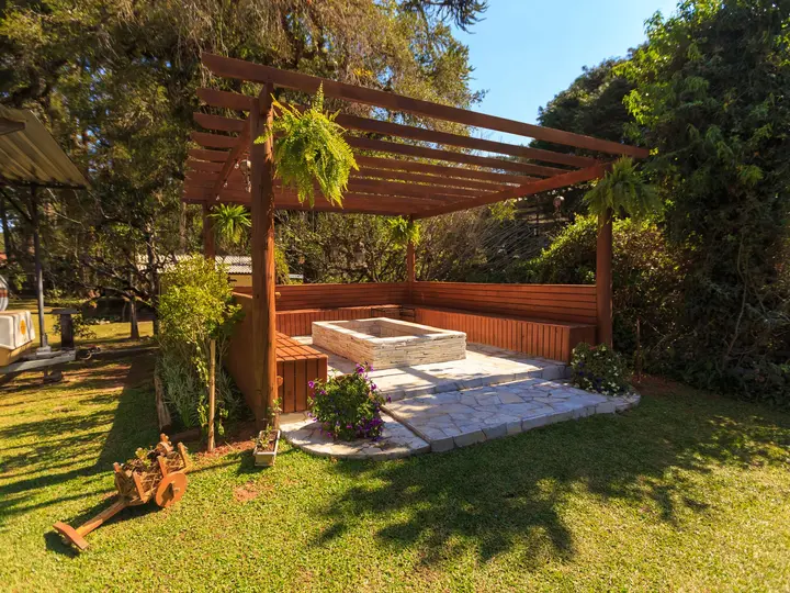 Wooden pergola over a paved seating area beside a lawn and mature trees